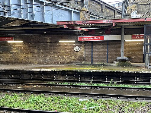 A platform at the closed King's Cross Thameslink station, brick wall, faded painted lettering and Do Not Alight Here signs, with weeds growing through the ballast.
