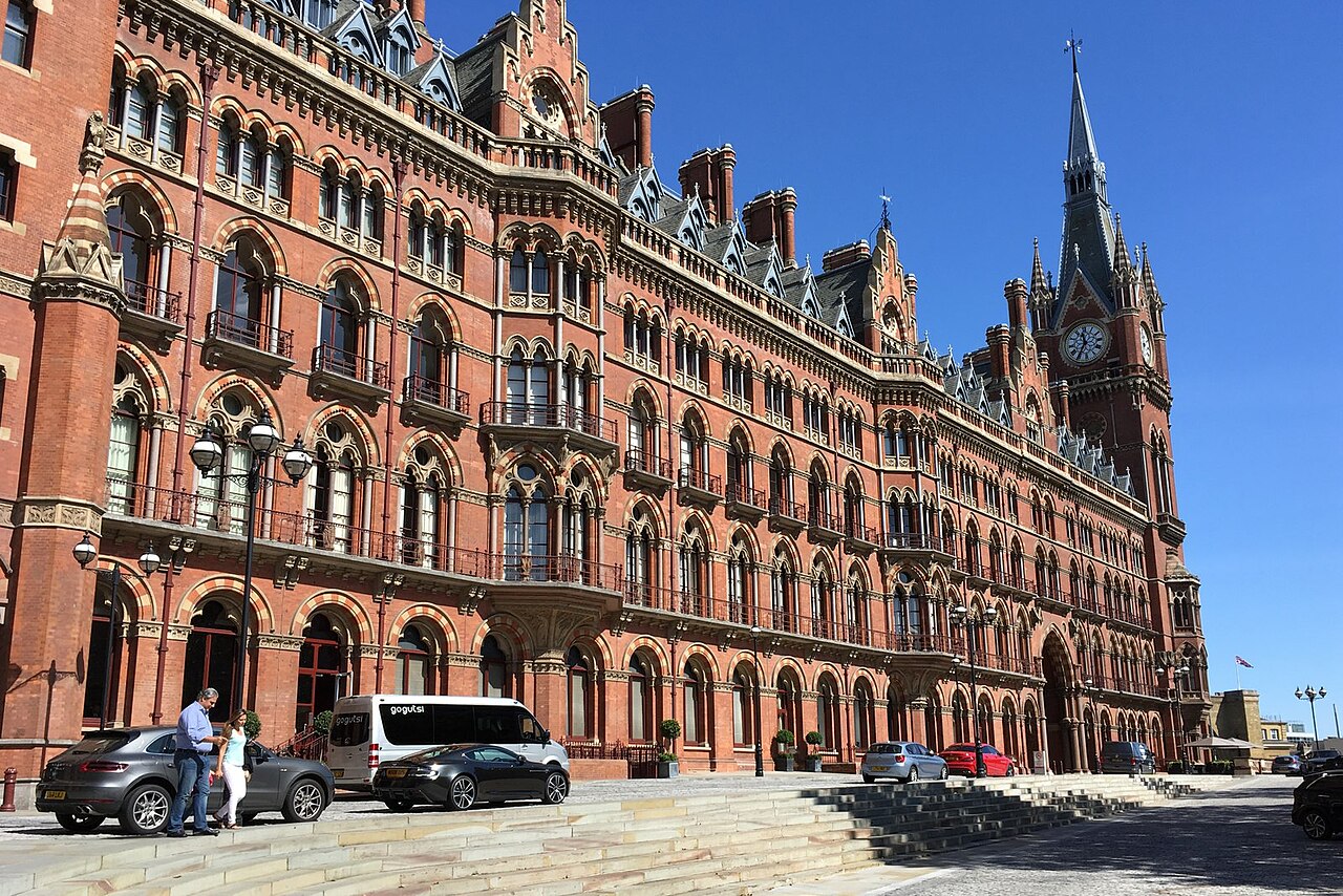 The red brick Gothic front of St Pancras on Euston Road in full sun, the clock tower at the far end and cars pulled up at the hotel entrance.