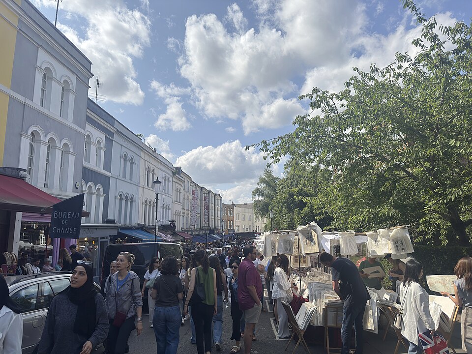 Portobello Road on market day, stalls and awnings, pastel terraces receding.
