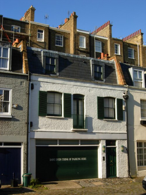 A cobbled mews of converted coach houses off Eccleston Square, white rendered fronts, green shutters and a garage door at street level.