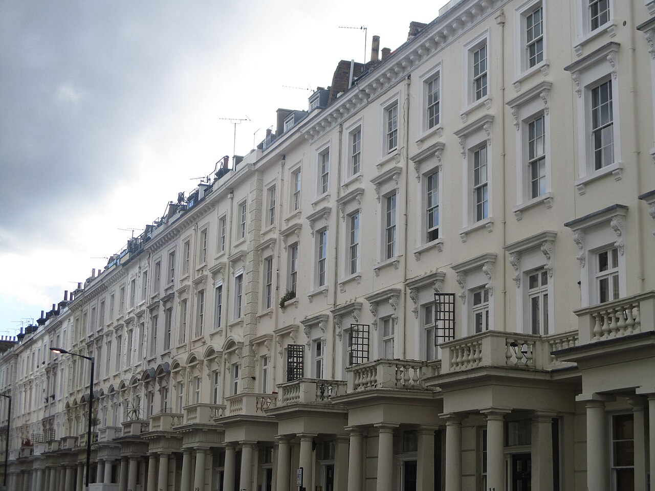 A long curving row of white stucco terraces receding down the block, with columned porches, balustraded balconies and repeated cornices.