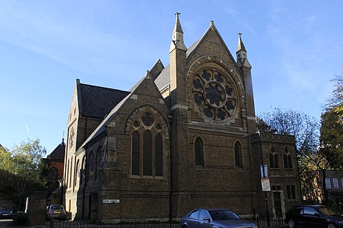 St Peter's London Docks from the corner of Raine Street, yellow stock brick with a rose window in the west gable and two small spirelets either side of it.