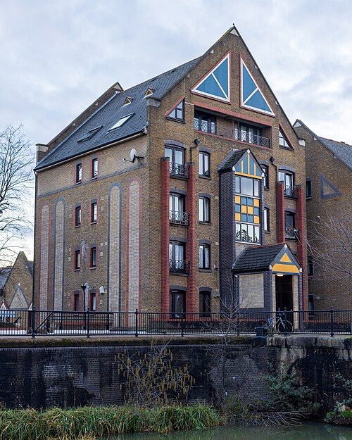 Flats on Discovery Walk above the canal, yellow stock brick with red brick pilasters and blue and yellow triangles painted in the gable.