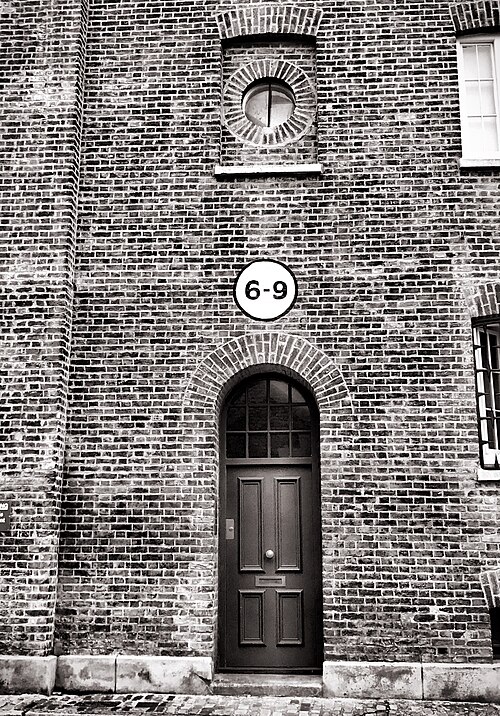 A stock brick warehouse front in black and white, a round bullseye window above an arched doorway with a painted 6-9 roundel between them.