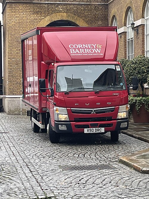 A wine merchant's lorry parked on granite setts in front of a stock brick building with a wide round arched opening and tall arched windows beside it.