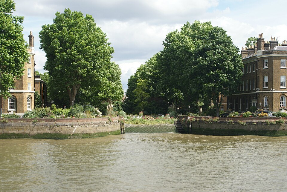 The two Pier Head terraces seen from the river, with a timber dam across the old basin mouth, steps at one end of it, and the garden and plane trees behind the wall.