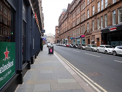 Albion Street from the pavement outside a bar, with red sandstone buildings along the far side and cars parked the whole length of it.