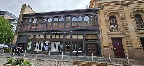The Scottish Music Centre front at 104 Candleriggs, a cast iron and glass arcade of round headed windows beside the sandstone flank of the City Halls.