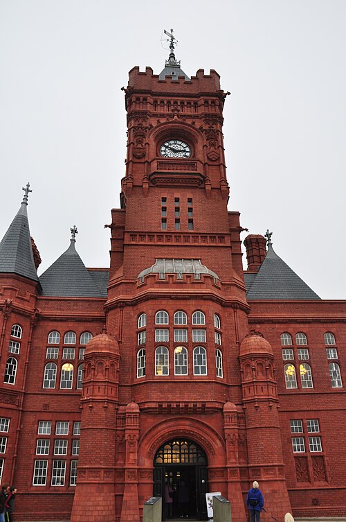 The Pierhead Building's red terracotta clock tower seen close up, arched windows and a weathervane above castellated turrets.