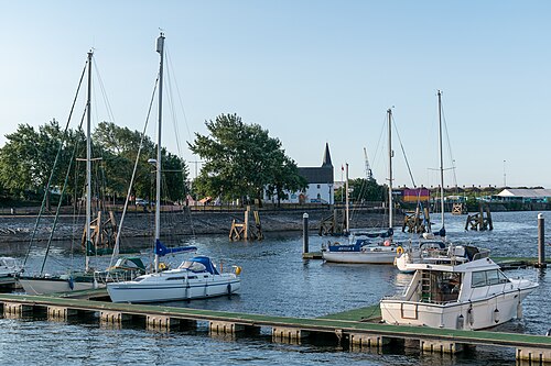 Yachts and motorboats moored at floating pontoons in the harbour, the white timber Norwegian Church visible across the water.