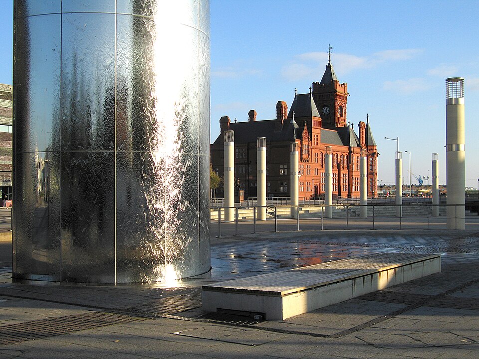The stainless steel water tower sculpture with water running down its sides, the red brick Pierhead Building visible across the plaza behind it.