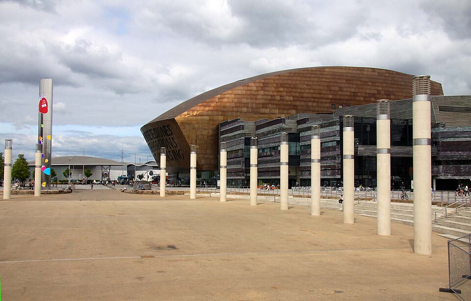 The Wales Millennium Centre's bronze steel dome and slate walls, viewed across Roald Dahl Plass with its row of steel light columns.