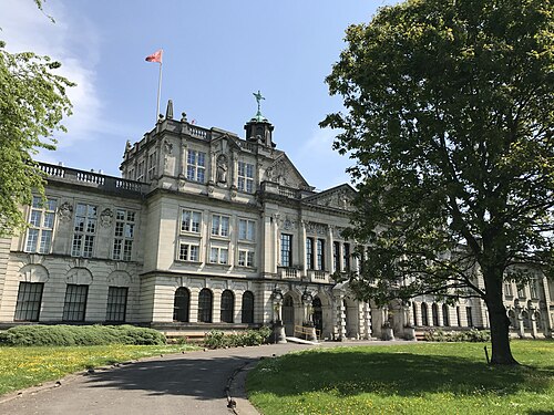Cardiff University's main building seen from Museum Avenue, an ornate corner tower with a winged figure on top, arched ground floor windows and a colonnade receding along the front.