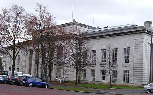 The Bute Building's plainer classical front with tall ground floor columns, parked cars along the kerb and bare trees in front.