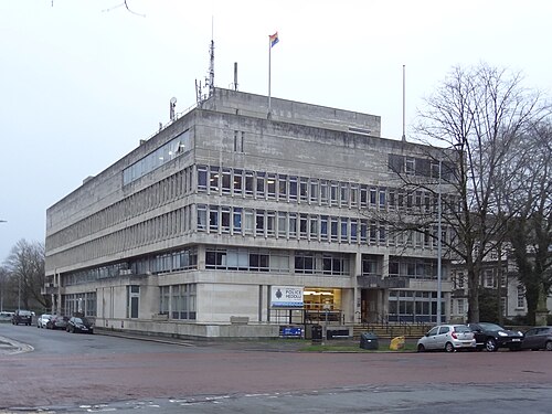 Cardiff Central Police Station, a tiered concrete block with ribbon windows and a Police Heddlu sign over the entrance, aerials on the roof.