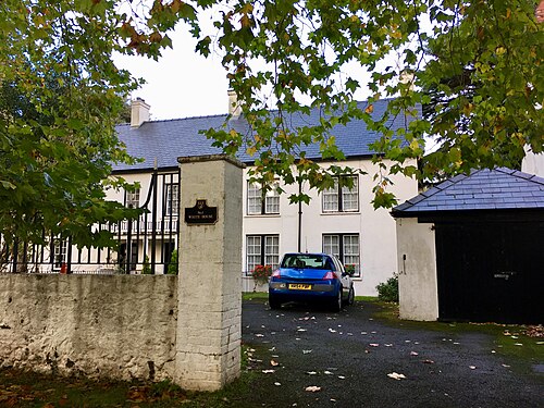 A pale rendered house behind iron gates and a stone gatepost inscribed White House, a car parked on the gravel drive under plane trees.