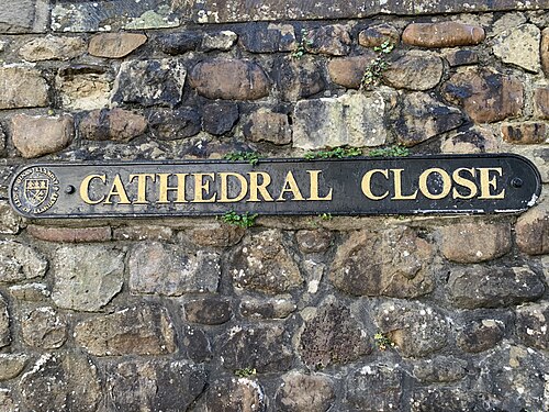 A cast metal Cathedral Close street sign bearing the City of Llandaff crest, fixed to a rubble stone wall.