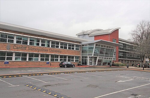 Cardiff Metropolitan University's Llandaff campus, a low brick building with a curved glazed entrance canopy behind an empty car park.