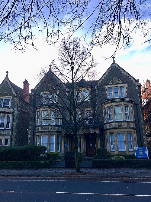 A three storey stone Victorian villa with twin gabled bays, bare winter tree branches in front, seen from across Cathedral Road.
