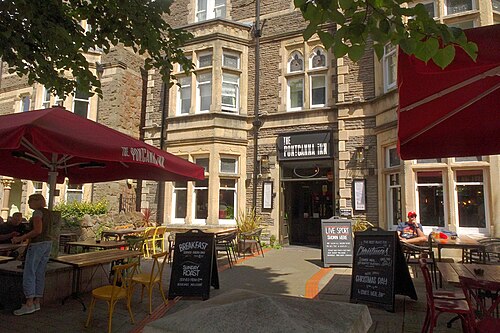 The Pontcanna Inn's stone corner gable and arched windows, red umbrellas and outdoor tables set out on the forecourt.