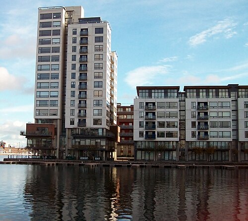 The Millennium Tower and an adjoining apartment block rising straight from the dock basin, with ground floor bars along the water's edge.