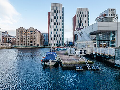 Boland's Flour Mills, a stone mill building with its original gable roofs and painted lettering, beside newer glass towers across the water.