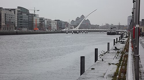 The Samuel Beckett Bridge's single white mast and cables over the Liffey, seen from the quay with mooring posts in the foreground.