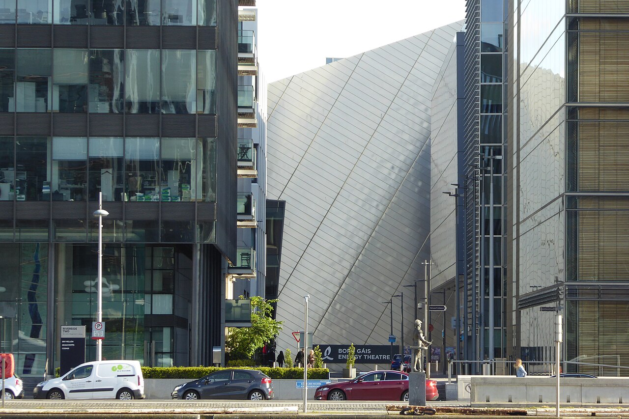 The Bord Gais Energy Theatre's glass front folded into sharp diagonal pleats, seen from the street between office blocks.