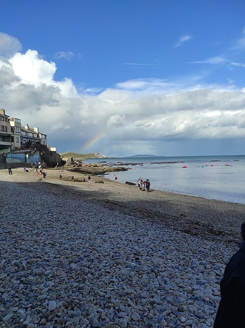 A pebble beach below Balscadden Road, guesthouses set into the cliff behind it.