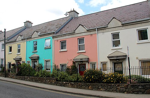 A row of two storey terraced houses on Abbey Street painted yellow, blue, pink and cream behind a low stone wall.