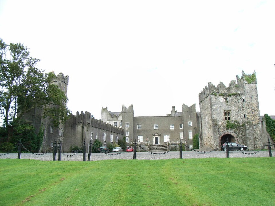The grey stone castle behind its lawn, battlements and rendered central facade with towers at each end.