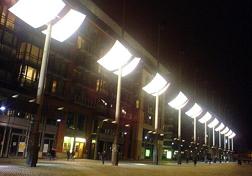 A row of the illuminated gas braziers on their masts along the square at night.