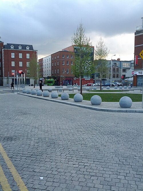 A wide stretch of the cobbled square with round stone bollards and multi storey brick buildings behind.