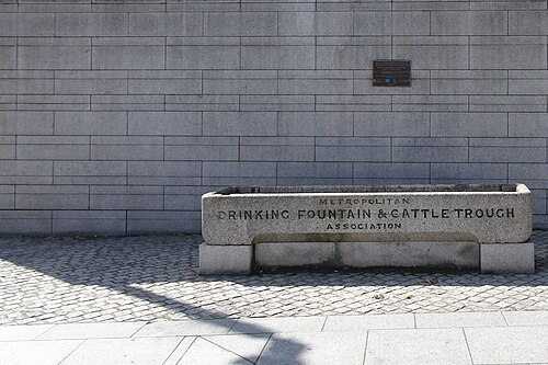 The Metropolitan Drinking Fountain and Cattle Trough, a carved stone trough set against a grey stone wall on the cobbles.