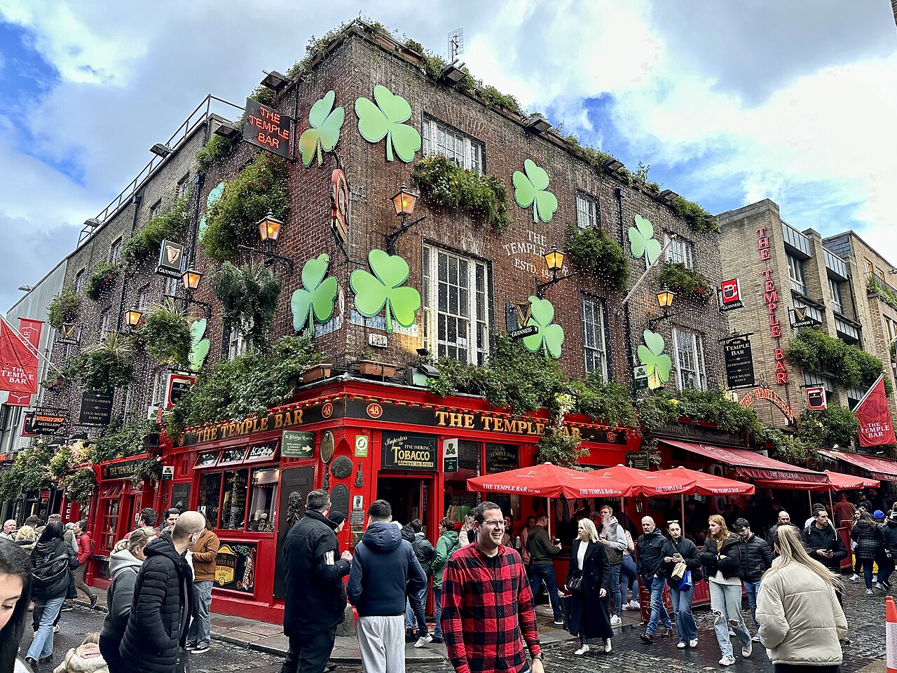 The Temple Bar pub on its corner, red paintwork, hanging flowers and a crowd outside.
