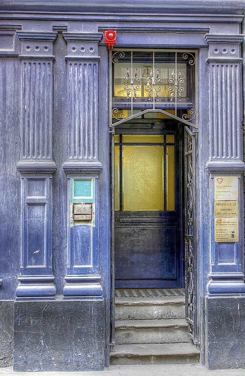 A blue painted timber doorway with wrought iron grilles and brass wall plaques.