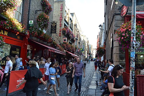 A cobbled lane lined with painted pub fronts and hanging flower baskets.