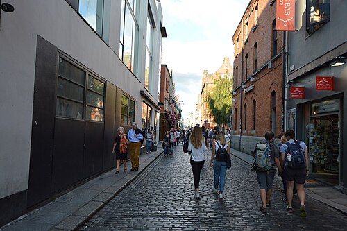 A cobbled lane where an older red brick terrace sits beside a modern glass fronted building.