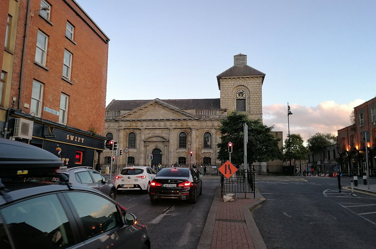 St. Catherine's Church stone tower closing the view down Thomas Street, traffic and a pub facade in the foreground.