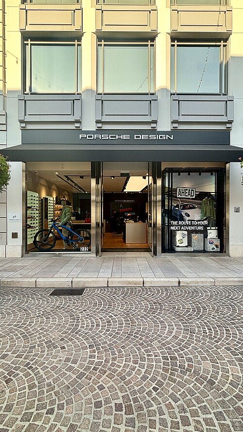 The Porsche Design storefront on Via Rodeo Drive's cobblestone, a bicycle and sunglasses displayed in the window.
