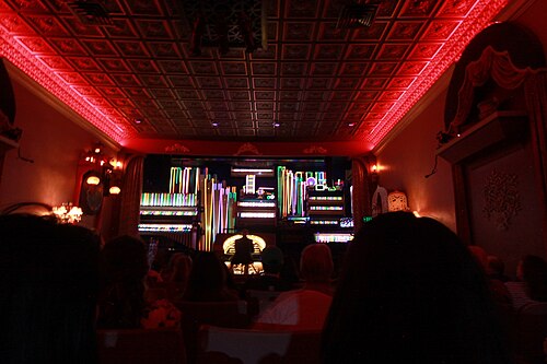 The theater's Wurlitzer organ pipes lit in color during a performance, the audience watching in silhouette.