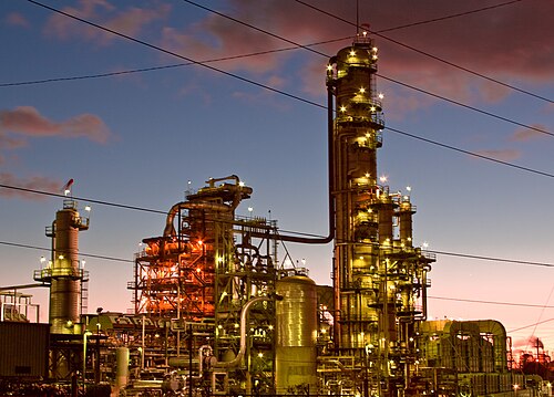 The Chevron refinery at dusk, towers and pipework lit up against the sky.