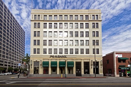 A cream stone bank building at a Brand Boulevard corner, six stories with arched ground floor windows and green awnings over the sidewalk.