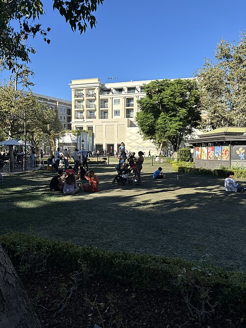 The Americana at Brand's central lawn, with a hotel building and Louis Vuitton and Bottega Veneta storefronts behind it.