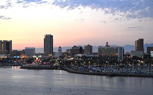 Downtown Long Beach's skyline at dusk, seen across Rainbow Harbor from the Queen Mary, a Ferris wheel and moored boats in front of the towers.