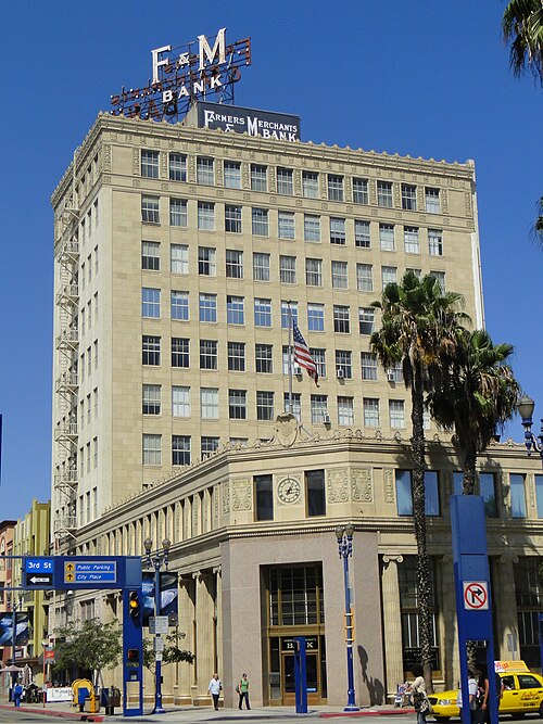 The Farmers and Merchants Bank building on Pine Avenue, its rooftop sign reading F and M Bank, seen from street level with a palm tree and a taxi at the kerb.