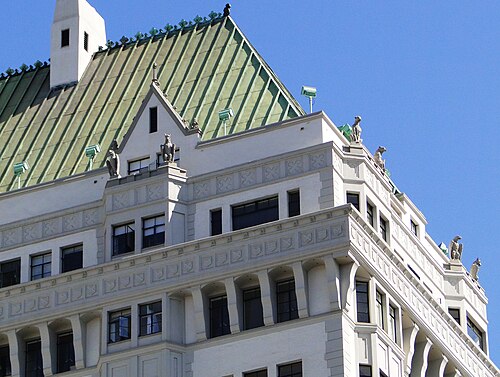 The green copper roof and carved grotesques at the top of the Villa Riviera apartment tower, seen close up against a clear sky.