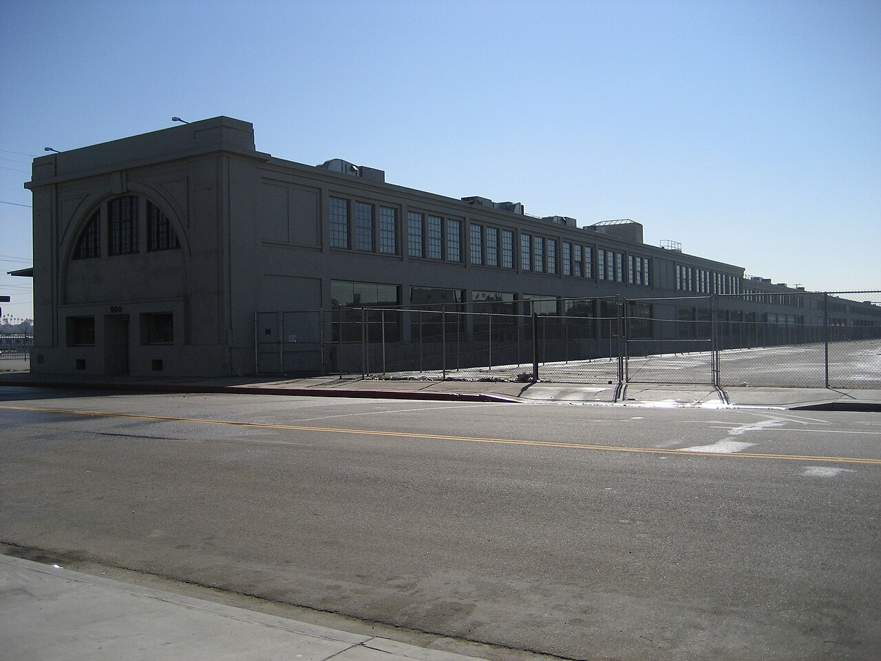 The former Santa Fe Freight Depot on East 3rd Street, a low warehouse addressed 960 stretching most of the block behind a chain link fence, on a wide empty street.