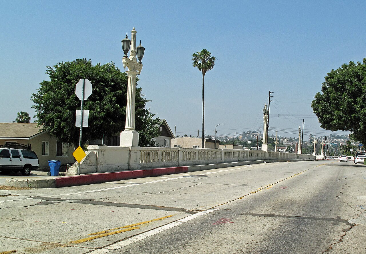 Lorena Street rising to the ornamented lamp posts and balustrade of a small bridge, houses and the hillside behind it.