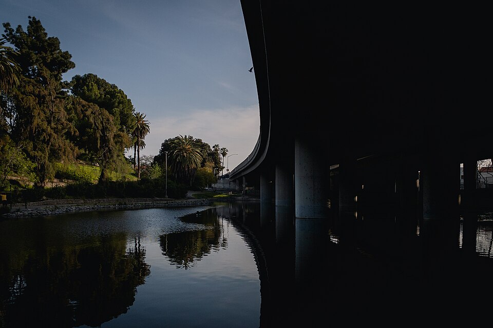 Hollenbeck Park's lake at dusk, a freeway ramp along the bank and palm trees on the far side.